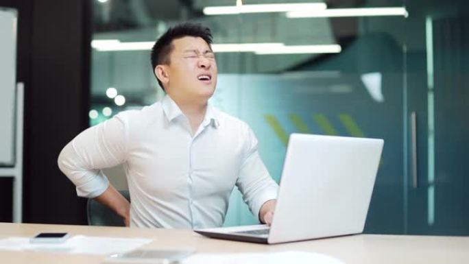 员工在工作场所有严重的背痛。在办公室工作的疲惫的商人长时间坐在电脑桌前