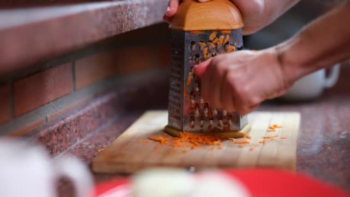 女人在刨丝器上手工切胡萝卜的特写镜头。