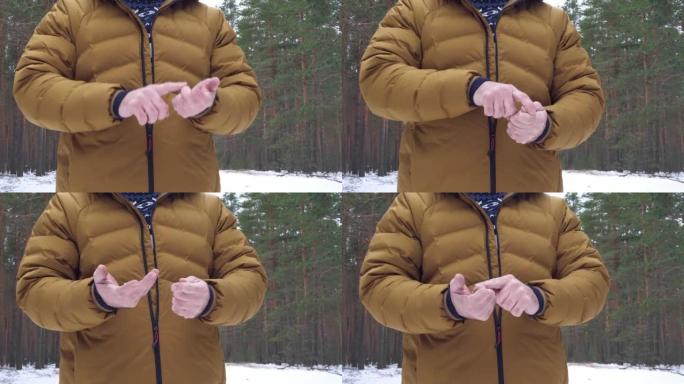 一个穿着芥末羽绒服的男人将手指弯曲在手上，在冬季森林中列出或数着东西。