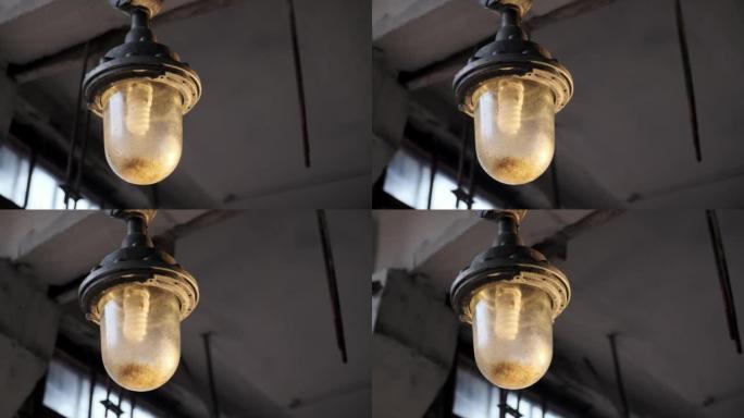旧废弃工厂天花板上悬挂的防爆灯。带大灯泡的不工作灯。黑暗中的光明概念。