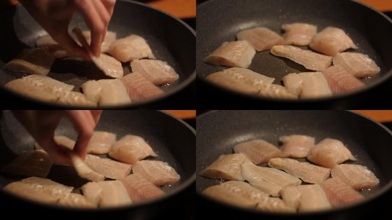 厨师放鱼。用油关闭煎锅的鱼片带鱼。烤健康食品。油炸鳕鱼片配香料特写。健康饮食欧米茄3。低热量白肉。