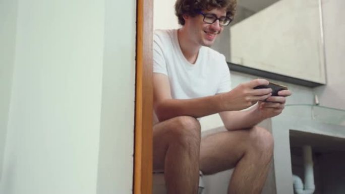 高加索帅哥玩家在家里用智能手机玩手机游戏。迷人的休闲男人感到快乐和放松，独自一人坐在手机上玩得开心，