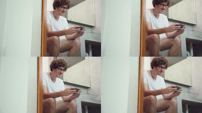 高加索帅哥玩家在家里用智能手机玩手机游戏。迷人的休闲男人感到快乐和放松，独自一人坐在手机上玩得开心，