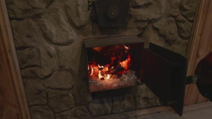 一个戴着特殊耐热手套的人的手打开了炉子上的金属门。柴火在烤箱里燃烧，煤在闷烧。炉火的概念。