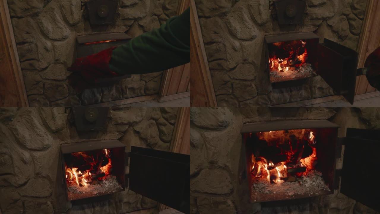 一个戴着特殊耐热手套的人的手打开了炉子上的金属门。柴火在烤箱里燃烧，煤在闷烧。炉火的概念。