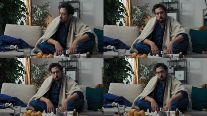 孤独的人生病了。他坐在沙发上体温。他有发热，所以男人被毯子覆盖。药品、苹果和一杯茶躺在桌子上。精疲力