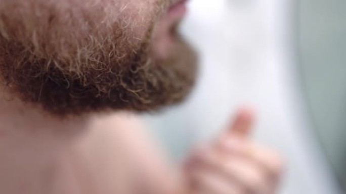 男子用手近距离触摸浓密的胡须，男子在镜子前的浴室里每天做面部护肤程序。每日刮胡子作为干燥或受刺激的面