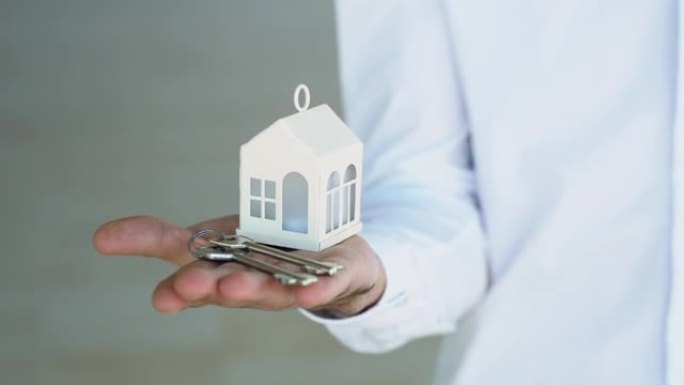 一名男子房地产经纪人手里拿着白宫模型和房子钥匙。按揭贷款审批房屋贷款及保险概念