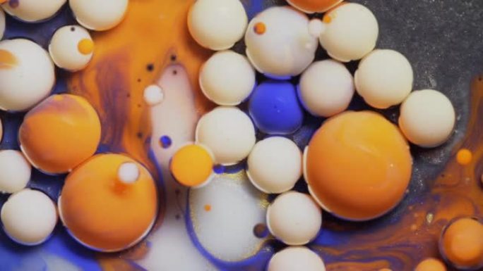 彩色的蓝色橙色和白色气泡散布在宇宙色彩表面，并混合在抽象设计中。金色闪闪发光的颗粒，墨球滴并在液体中