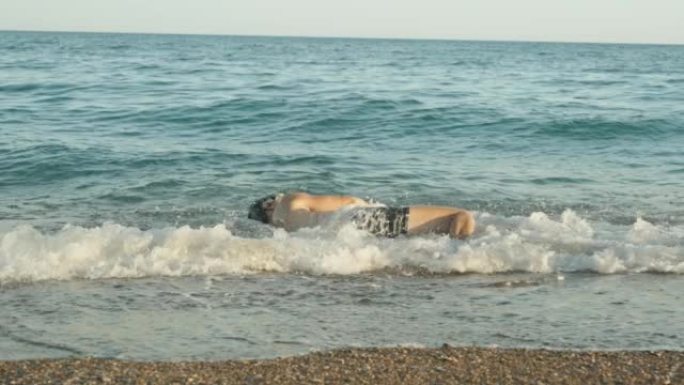 一名戴着潜水面具的男子沿着海边滚入水中，被海浪覆盖。慢mo