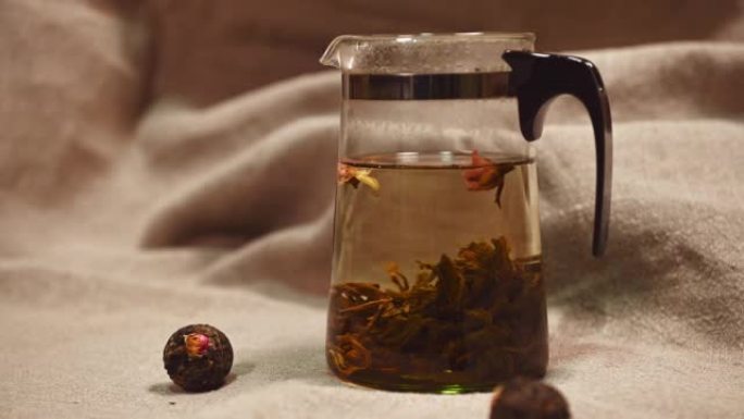 特写: 一团绿色的中国香茶与开水的透明茶壶中的开口花