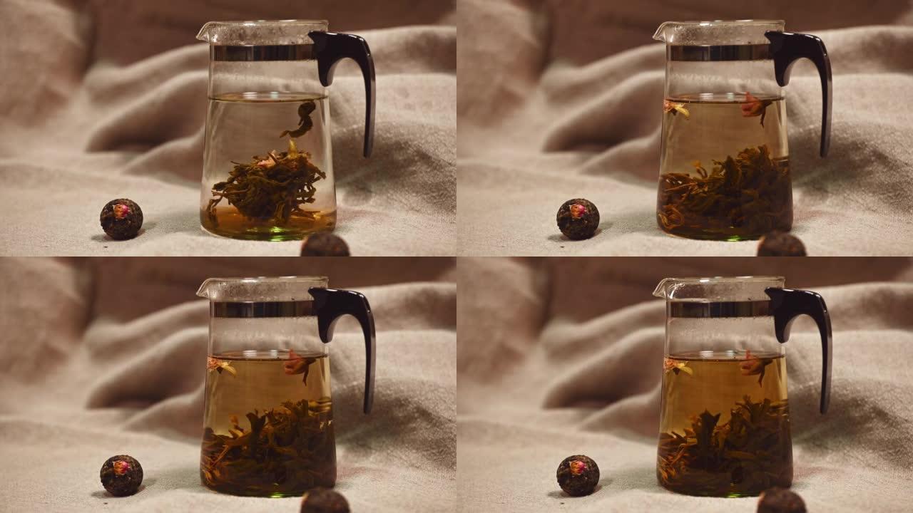 特写: 一团绿色的中国香茶与开水的透明茶壶中的开口花