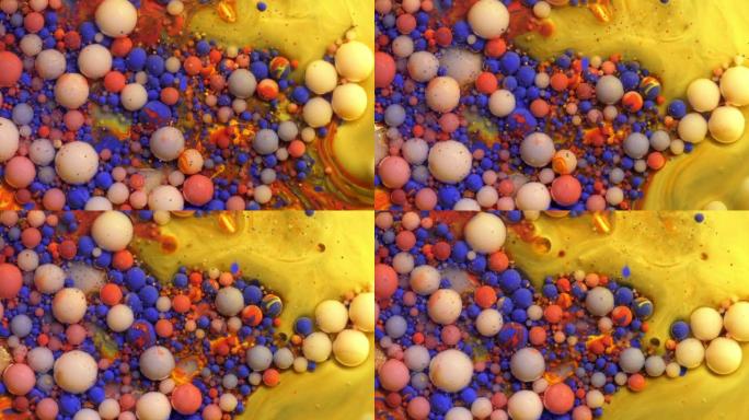 彩色丙烯酸红色和蓝色油漆气泡散布在黄色表面混合在抽象设计中。金色闪闪发光的颗粒，墨球滴和混合。运动中