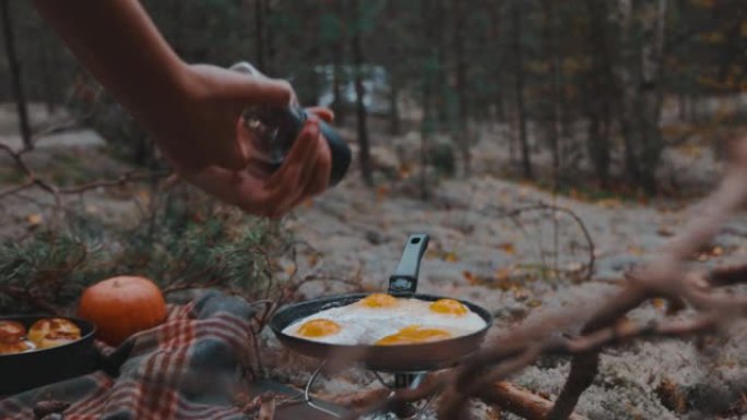 在森林里野餐时，双手慢动作用黑胡椒粉煎鸡蛋