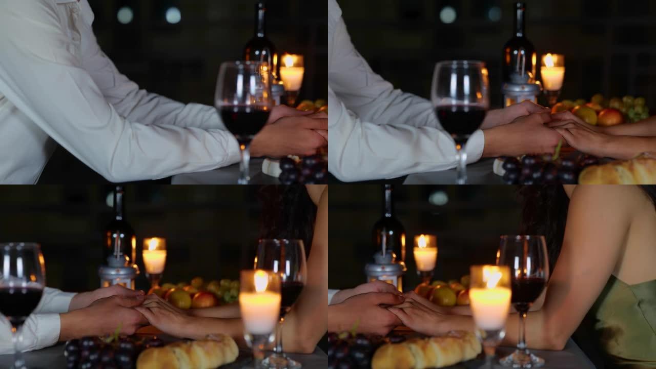 情人在晚上牵手约会的特写镜头。恋爱中的男人和女人手牵手坐在户外的餐桌旁，蜡烛和美酒。浪漫晚餐。爱情关