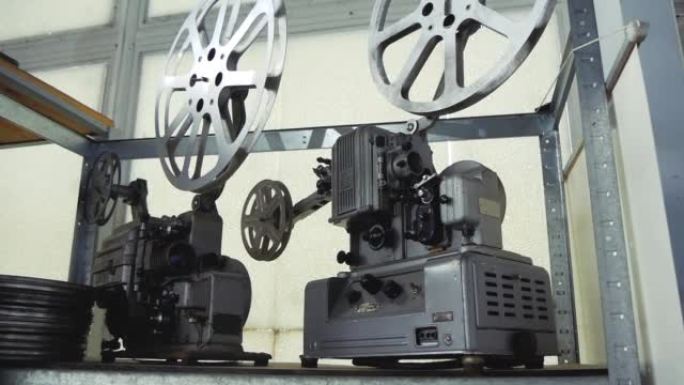 两个老式电影放映机和一盒放在架子上的电影