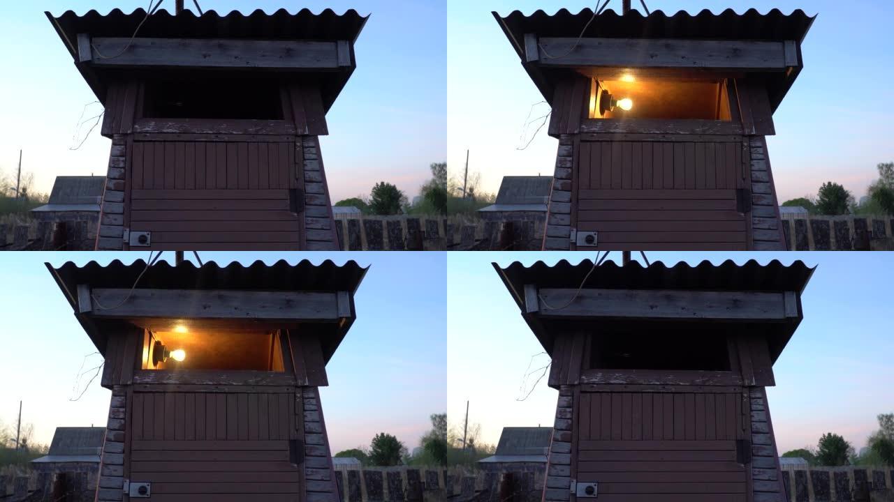后院的农村木制厕所。打开和关闭电，灯泡。日落之后的厕所映衬着蓝色的黑暗天空。