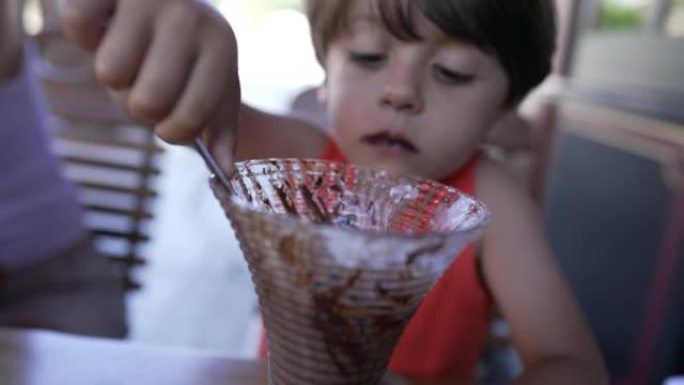 孩子在餐厅用勺子吃巧克力冰淇淋。小男孩吃糖甜点