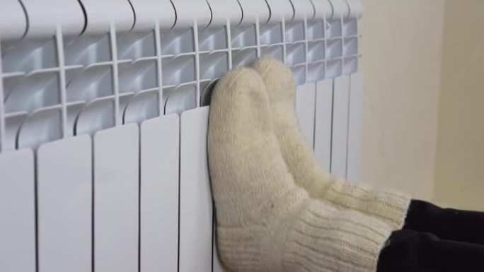 女孩在暖暖的暖气片上暖腿。女性腿的特写穿着白色羊毛袜送到散热器。4 k