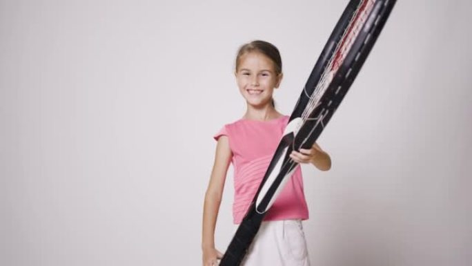拥有超大球拍的年轻女子网球运动员。穿着粉色运动服的女孩微笑着摆姿势。