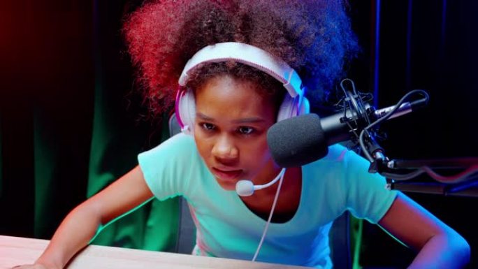 年轻的非洲裔美国妇女戴着耳机玩视频游戏和在线直播与麦克风在家里，游戏和esport或演员游戏，一个人