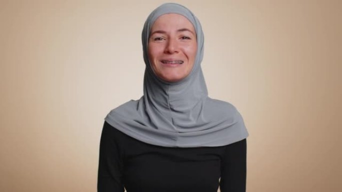戴着头巾的穆斯林妇女在镜头前友好地微笑着，点头示意你好，阿萨拉穆·阿莱库姆