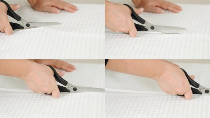 一位女裁缝在桌子上剪了一块白色布料。