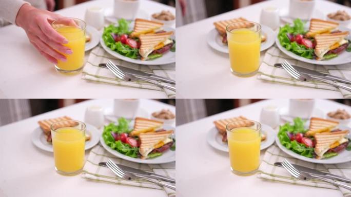 美味的早餐 -- 女人把一杯新鲜的橙汁放在桌子上，上面放着三明治
