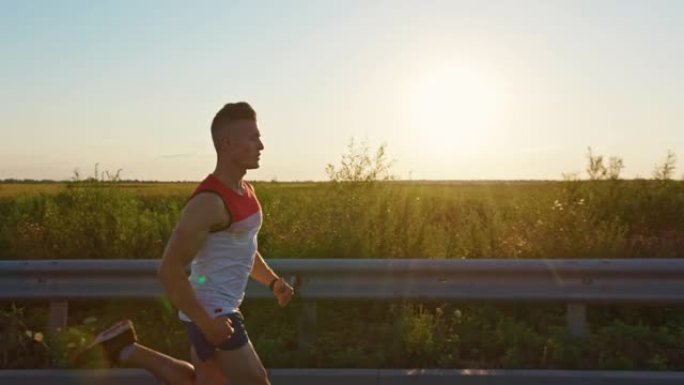 强壮的男人穿着运动服，日落时在马路上快速奔跑。
