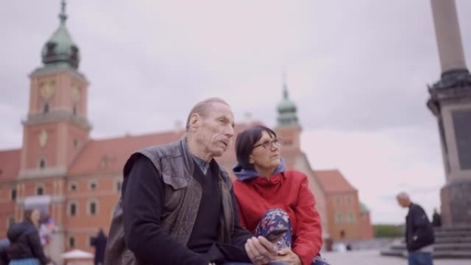 老年游客夫妇坐在欧洲古城的历史中心聊天。华沙老城皇宫广场