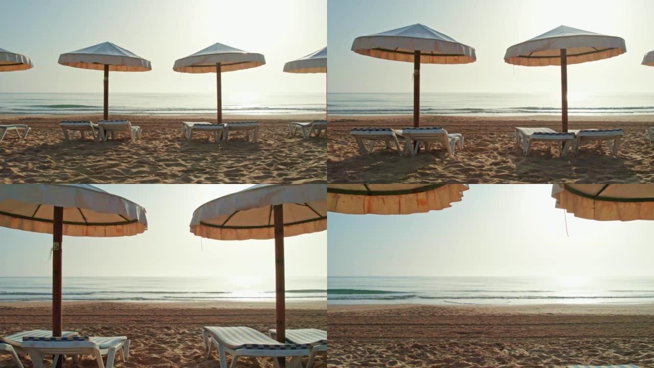 为泳客准备的雨伞和沙滩椅。日出。清晨的海滩。早晨的阳光下，夜间在海滩上耙沙的痕迹。雨伞之间的前向摄像