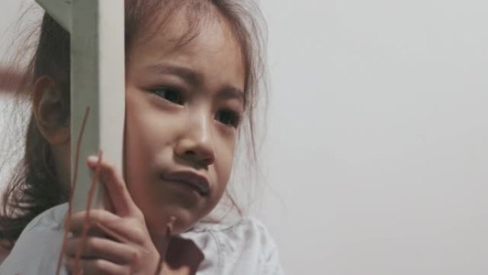 可爱的亚洲女孩的特写脸独自在房子的楼梯上表达她的悲伤情绪，表现出抑郁、情感痛苦和孩子不快乐的概念，这