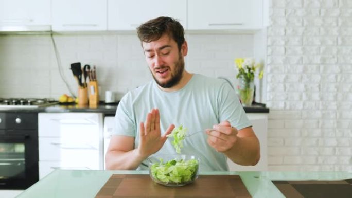 一个年轻人用一只手拿着叉子和沙拉，另一只手显示停止饮食