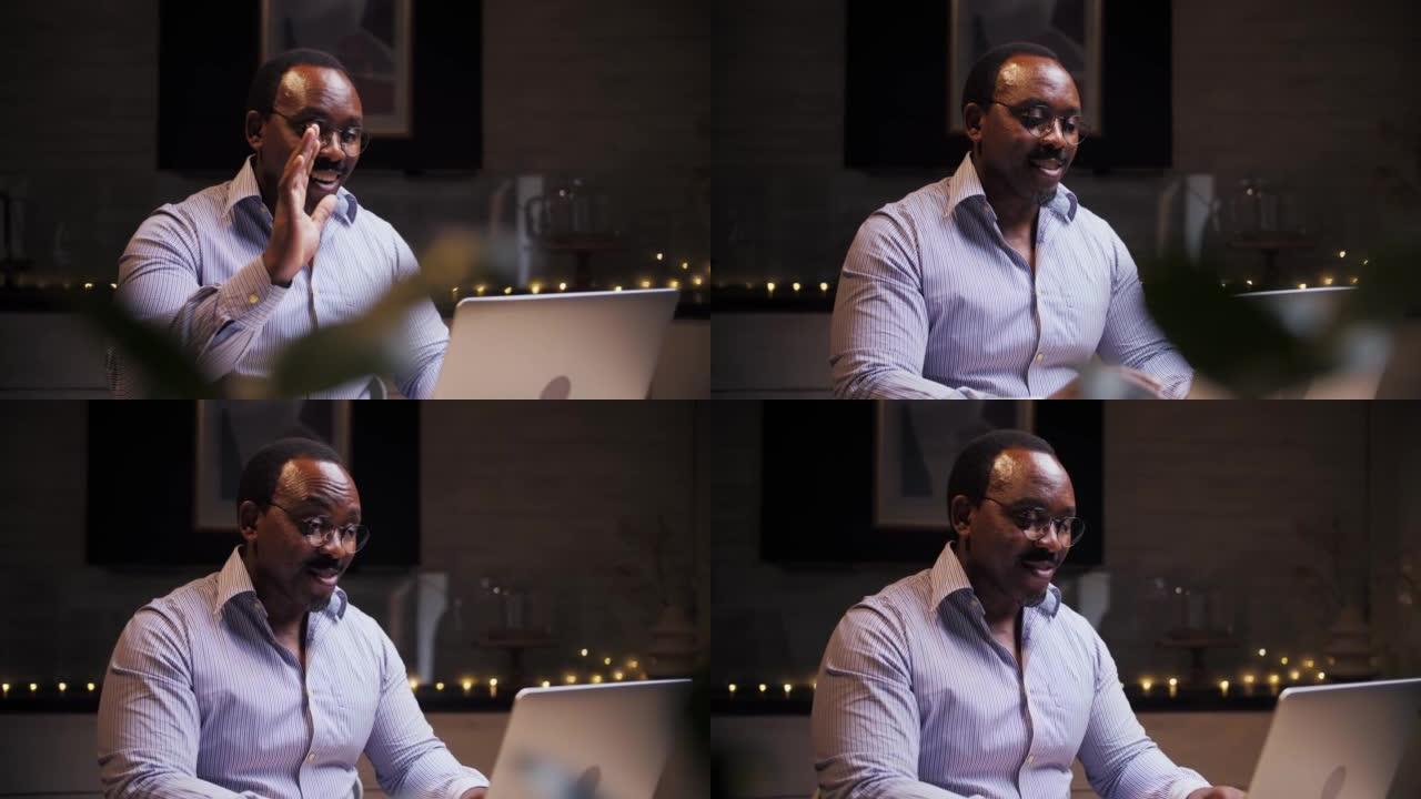 非洲男子坐在家里用笔记本电脑做视频通话。商务人士看着电脑进行在线交流。年轻微笑的男性和朋友见面。