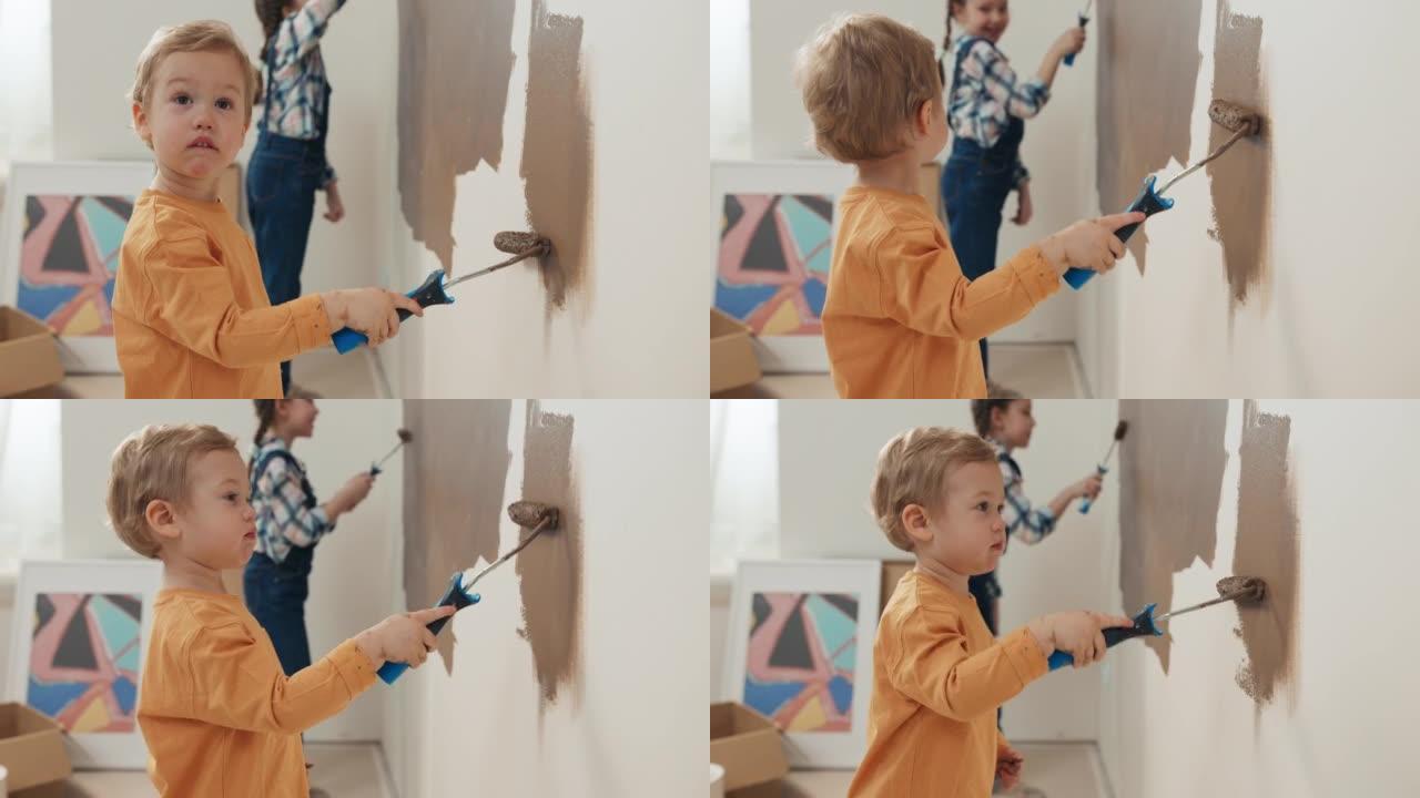 穿着橙色毛衣的小男孩手里拿着滚筒，把墙壁涂成棕色。这个男孩有一头金发，看着从侧面画画的姐姐。扎着辫子