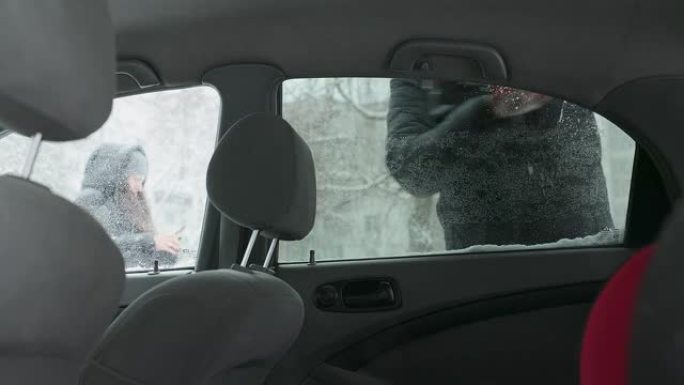 车主将汽车后门的窗户从雪地上清洗干净。