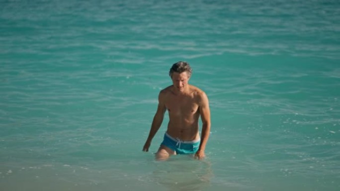 游泳后，肌肉发达的人在爱琴海Oludeniz海滩的地中海绿松石海水中的海滩上慢动作。夏季旅游季节费蒂