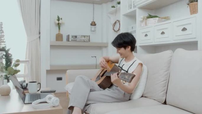 一名亚洲年轻女子在家沙发上弹吉他