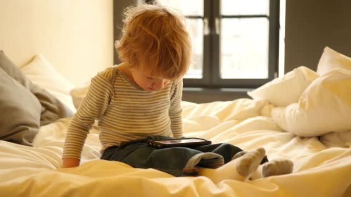 可爱的小男孩坐在床上看智能手机卡通