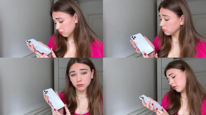 年轻女子带着困扰的表情，手里拿着她破碎的触摸屏手机破碎的智能手机深色头发和粉色衬衫的女孩手机白色