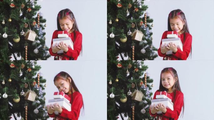 快乐的亚洲小女孩微笑着在圣诞树附近赠送圣诞礼盒。快乐的小女孩和礼物。寒假