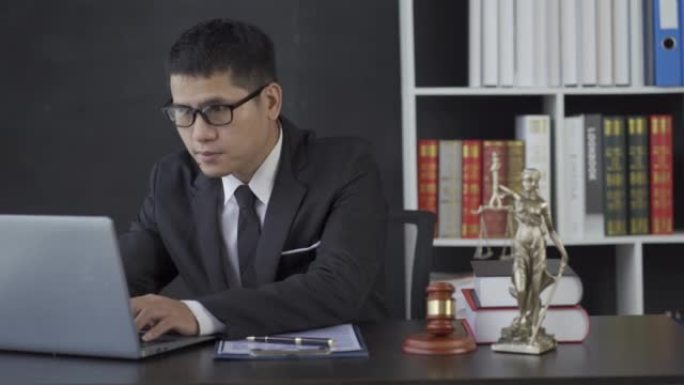 亚洲男性律师工作与锤子笔记本电脑正义女神在律师事务所，在线咨询的概念。