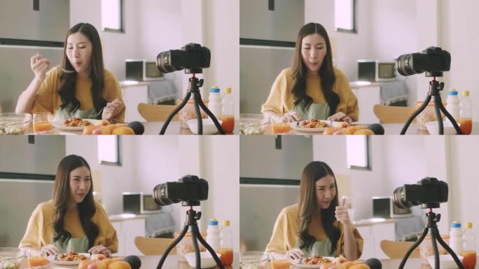 年轻微笑的美女影响者食物博主拍摄视频，在家里的厨房里用相机吃意大利面。社交媒体影响者概念。