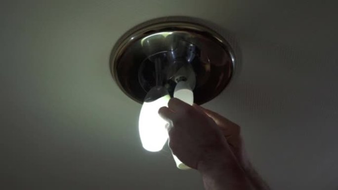 男人的手正在将节能灯泡拧入天花板上的小灯中。