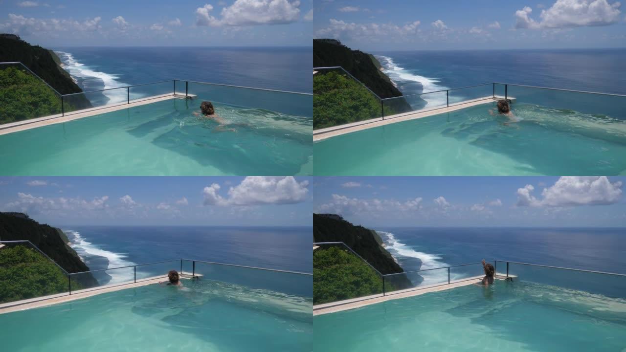 一流假期的豪华度假胜地的概念。一名年轻女子在无边泳池游泳，可以看到令人叹为观止的海景。她在蔚蓝的水中