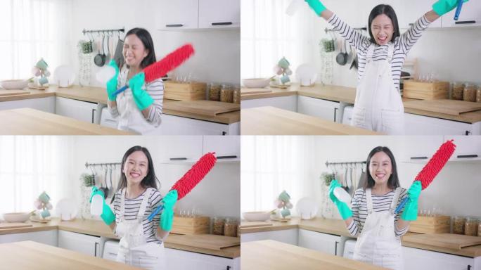 年轻快乐的亚洲妇女一边打扫家庭，一边举起手来争取成功和成就。漂亮的清洁服务工人家政和整理厨房。家务和