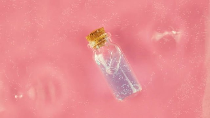 粉红色背景上的化妆品瓶，水滴上的瓶子。水波运动缓慢。设计、广告、产品