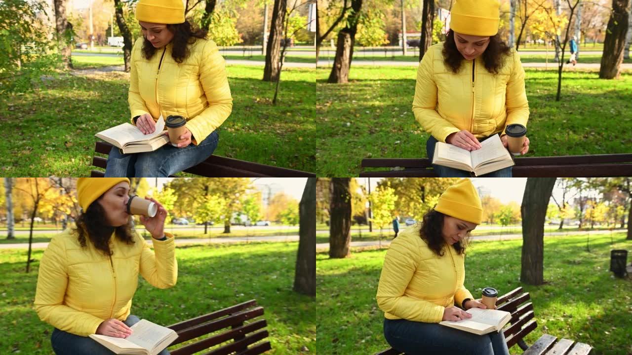 穿着黄色夹克的迷人女人，从纸杯里喝外卖咖啡，看书，坐在秋季公园的长凳上