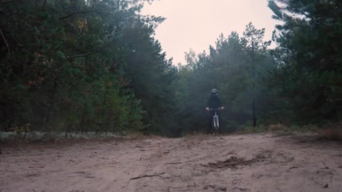 在一辆山地自行车上，一名男子沿着森林土路爬上小山，在镜头前急刹车，然后继续骑行。一个穿着运动服和头盔