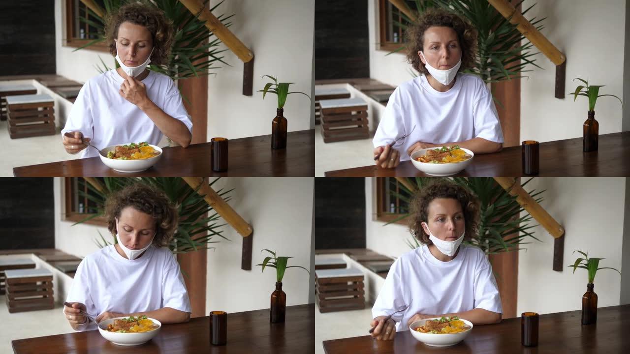 在新型冠状病毒肺炎大流行期间，孤独的年轻女子独自吃素食午餐。在开始进食之前，她将面罩拉到下巴上，但没